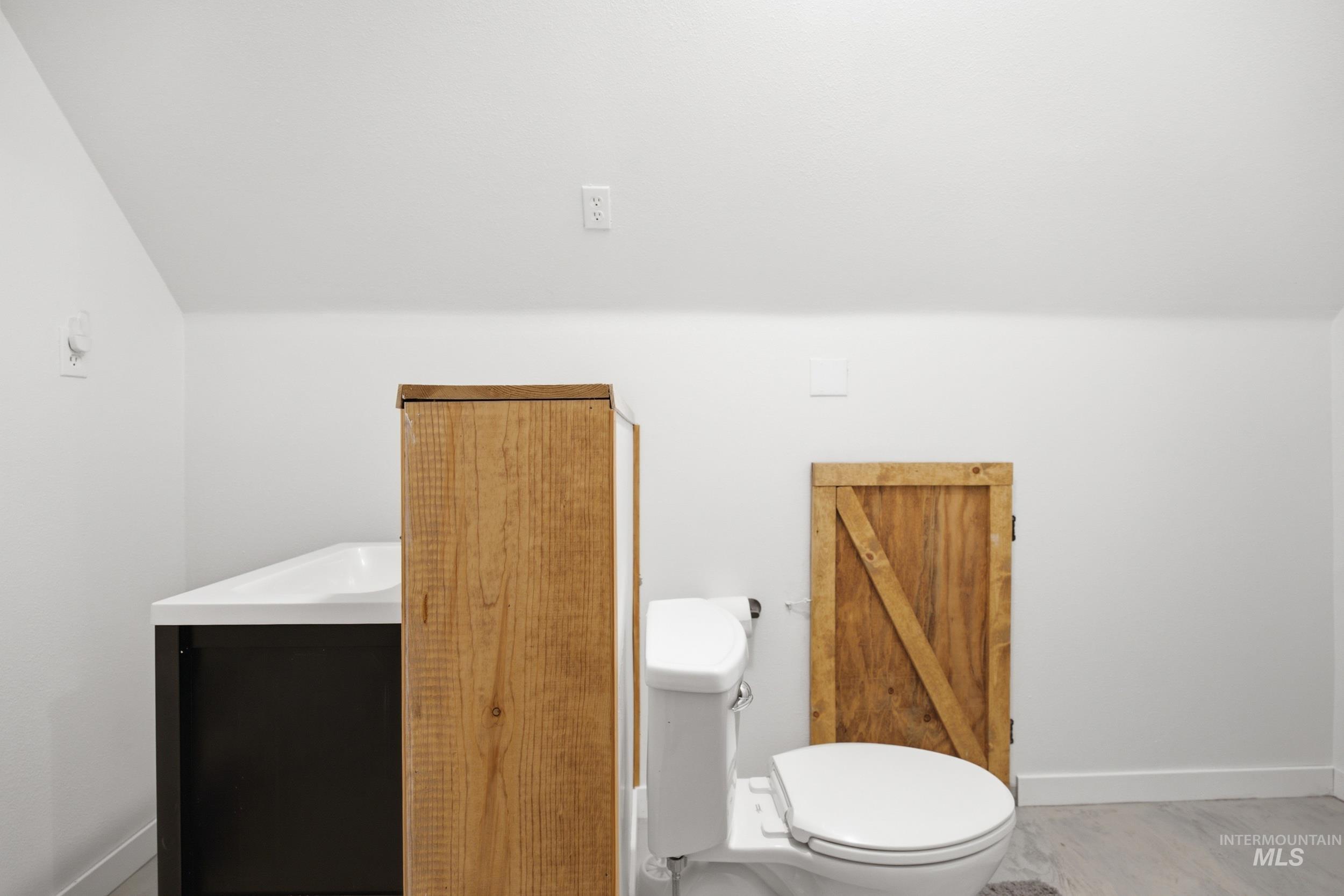3980 North Pine-Featherville Road Mountain Home, ID 83647 - Photo 28 of 35 Contemporary bathroom featuring a white toilet, black vanity with an integrated white sink, and a rustic wood-finish storage cabinet