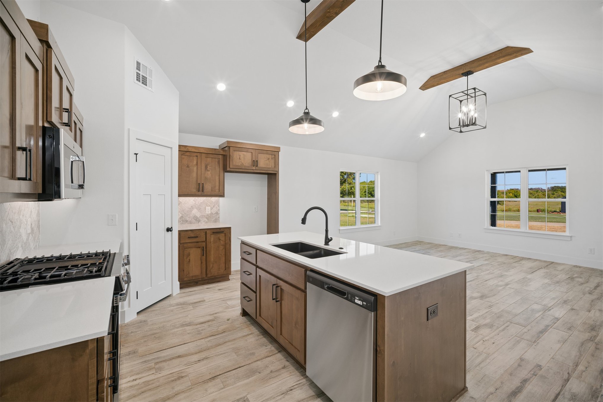 25036 South 4205 Road Inola, OK 74036 - Photo 11 of 30 Vaulted ceiling with exposed wood beams, wood-finish flooring, central kitchen island with integrated sink, stainless steel appliances, and wood cabinetry