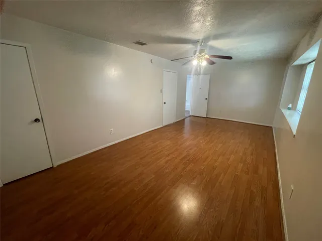 an empty room with wooden floor and fan
