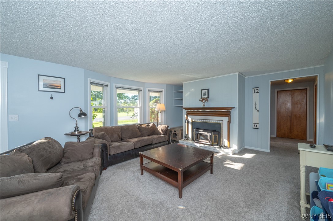 6463 Ward Road Sanborn, NY 14132 - Photo 6 of 49 Sunlight streams through bay windows into a comfortable living room featuring a classic wood-burning fireplace.