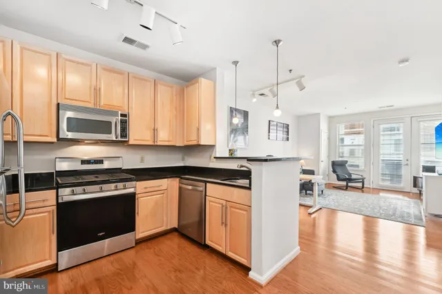 a kitchen with stainless steel appliances granite countertop a stove top oven a sink dishwasher a refrigerator and white cabinets with wooden floor