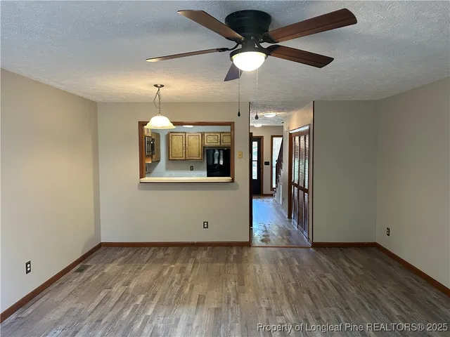 an empty room with wooden floor chandelier fan and kitchen view