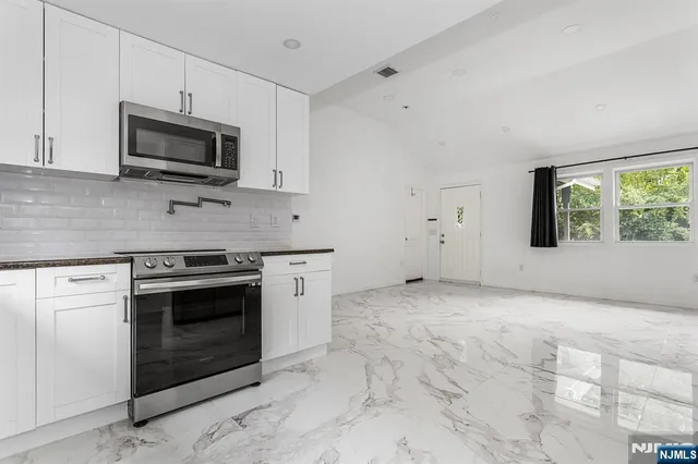 a kitchen with granite countertop a stove a microwave and white cabinets