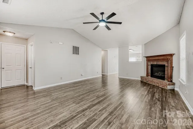 an empty room with wooden floor a ceiling fan a fireplace and windows