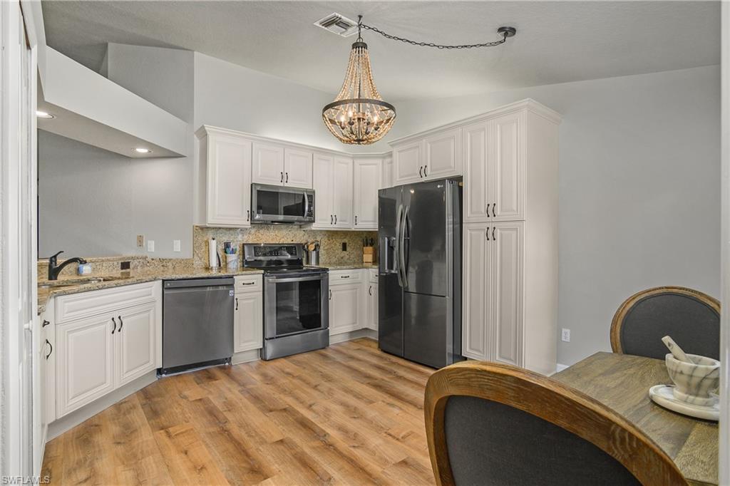 13061 Hamilton Harbour Drive, Unit R1 Naples, FL 34110 - Photo 9 of 23 Kitchen featuring stainless steel appliances, white cabinetry, decorative backsplash, light wood-style flooring, and light stone counters
