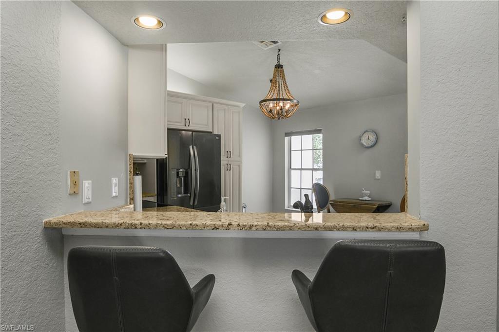 13061 Hamilton Harbour Drive, Unit R1 Naples, FL 34110 - Photo 10 of 23 Kitchen featuring a textured wall, a textured ceiling, light stone counters, stainless steel refrigerator with ice dispenser, and pendant lighting