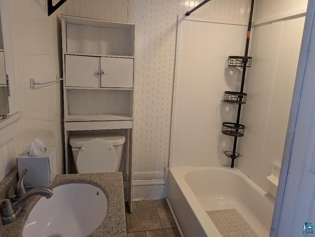 513 South Main Street Mellen, WI 54546 - Photo 10 of 22 Bathroom featuring a white bathtub with a shower kit, a toilet with an over-the-toilet storage unit, a vanity with a drop-in sink, and a speckled countertop
