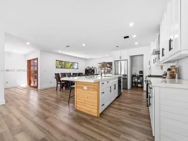 a large white kitchen with wooden floors stainless steel appliances and view living room