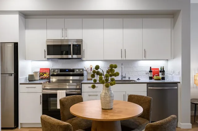 a kitchen with stainless steel appliances a white kitchen island a stove a microwave a sink a refrigerator dining table and chairs