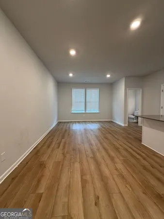an empty room with wooden floor and kitchen view
