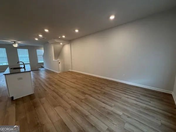 an empty room with wooden floor and a kitchen view