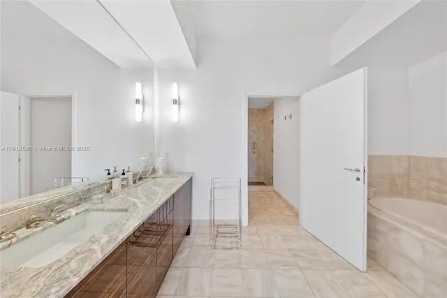 a spacious bathroom with a granite countertop double vanity sink a mirror and a bathtub