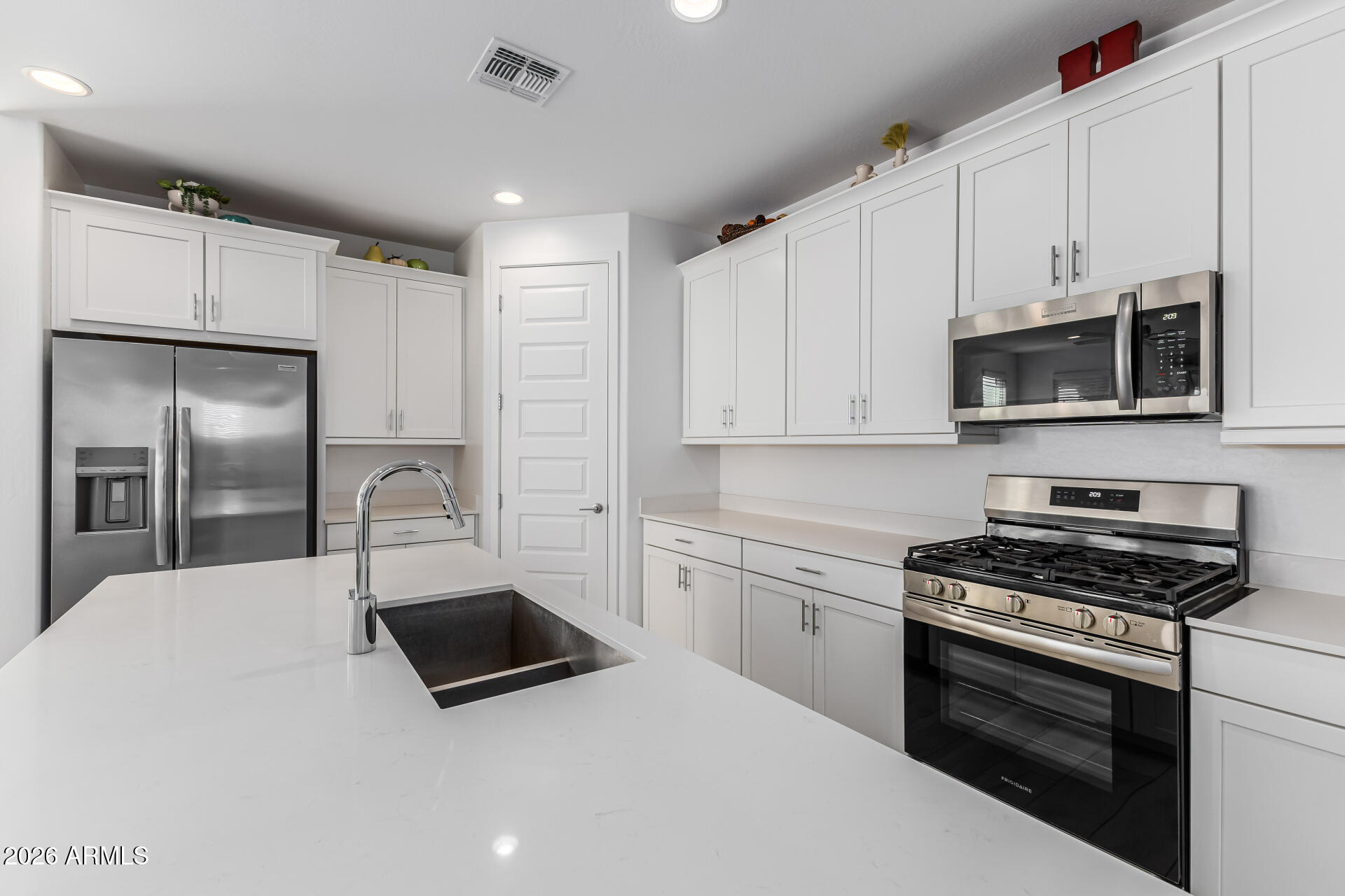 3347 South 156th Avenue Goodyear, AZ 85338 - Photo 16 of 50 a kitchen with granite countertop a refrigerator a sink a stove and white cabinets