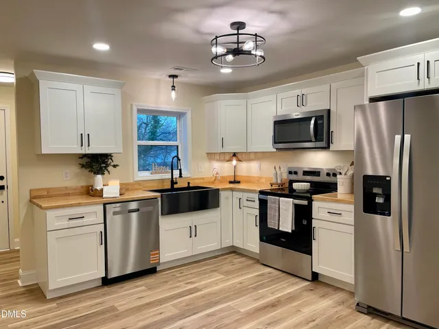 a kitchen with stainless steel appliances granite countertop a stove top oven a refrigerator a sink and dishwasher with wooden floor