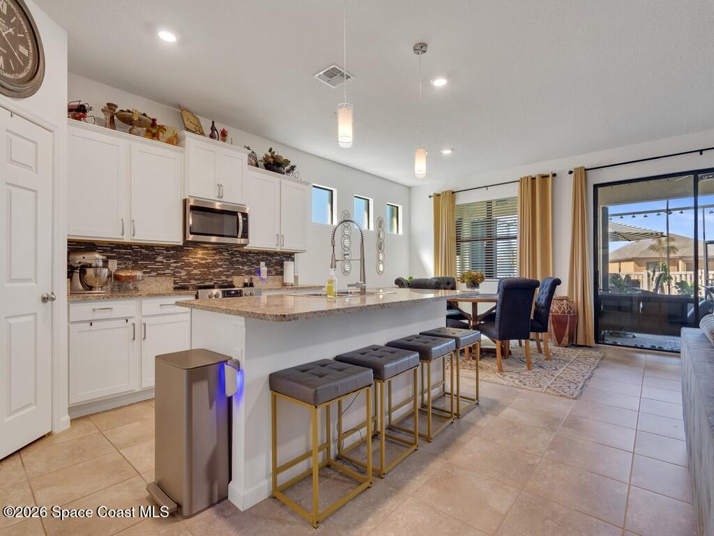 645 Old Country Rd S East Palm Bay, FL 32909 - Photo 2 of 42 a kitchen with stainless steel appliances granite countertop a stove top oven a sink dishwasher a dining table and chairs with wooden floor
