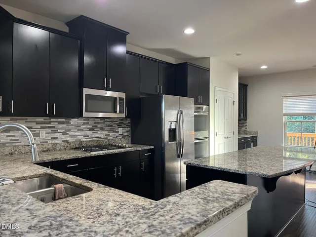 a kitchen with stainless steel appliances kitchen island granite countertop a sink and a refrigerator