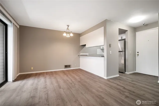an empty room with wooden floor and a kitchen
