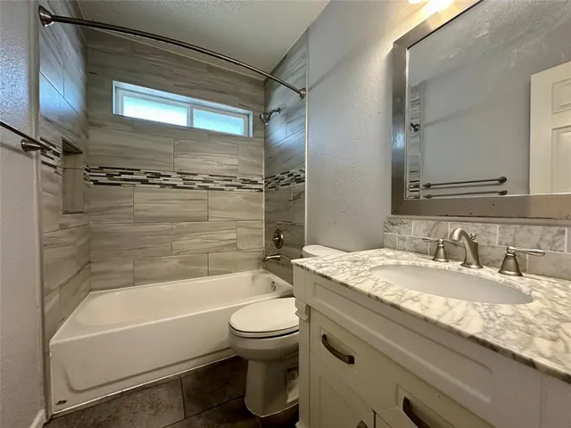 a bathroom with a granite countertop bathtub shower sink vanity and toilet