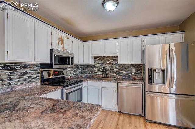 6773 Dale Road Colorado Springs, CO 80915 - Photo 11 of 45 Kitchen featuring tasteful backsplash, a sink, light wood finished floors, white cabinets, and appliances with stainless steel finishes