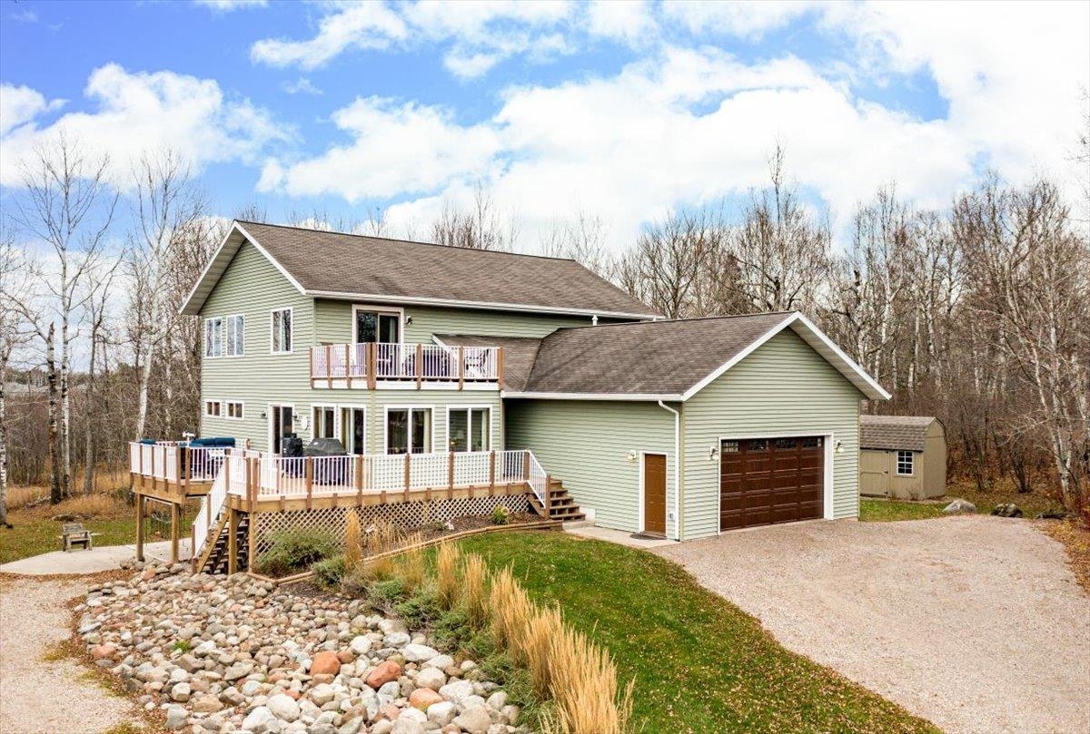 View of front of property featuring roof with shingles, driveway, a wooden deck, stairway, and a garage