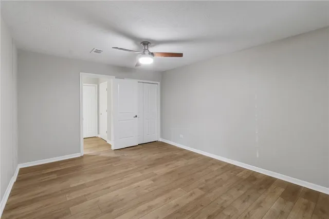 an empty room with wooden floor fan and windows