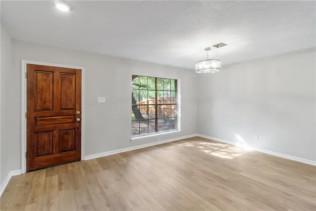 an empty room with wooden floor chandelier and windows