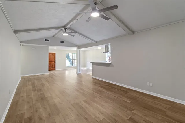 an empty room with wooden floor ceiling fan and windows