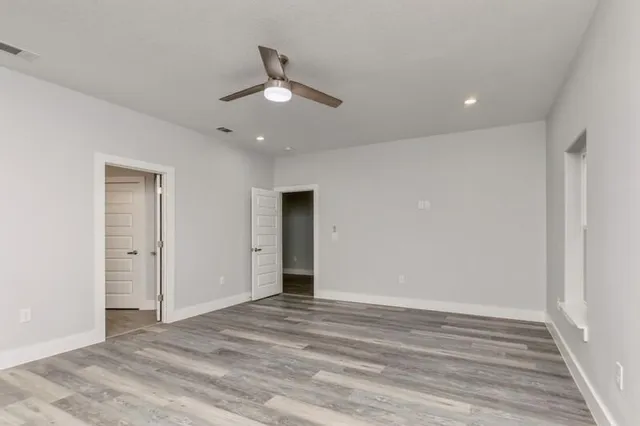 an empty room with wooden floor fan and windows