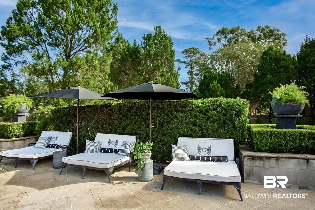 150 Austill Avenue Mobile, AL 36608 - Photo 36 of 39 Expansive stone patio featuring manicured hedges, mature trees, and a decorative urn with plantings