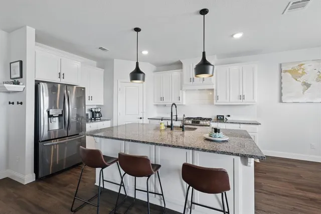 a kitchen with stainless steel appliances granite countertop a sink a stove a refrigerator and wooden floor