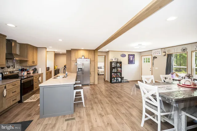 a living room with stainless steel appliances kitchen island granite countertop a kitchen island a stove a sink dishwasher and a dining table with wooden floor