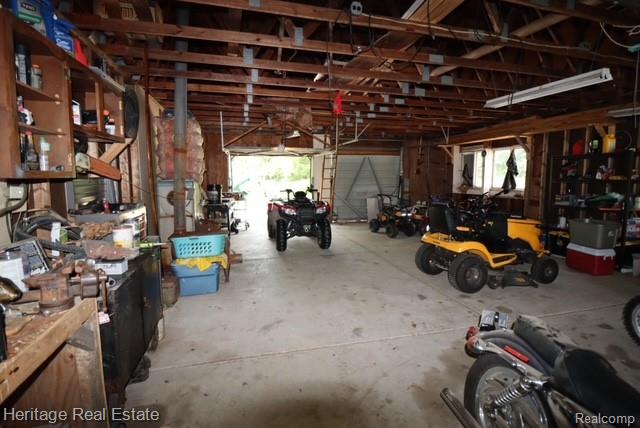 445 Mack Road Leonard, MI 48367 - Photo 20 of 41 Spacious garage featuring exposed wood beam ceiling, concrete flooring, and multiple storage options including built-in shelving and workbenches
