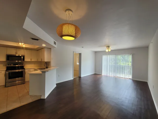 a view of an empty room and kitchen with wooden floor