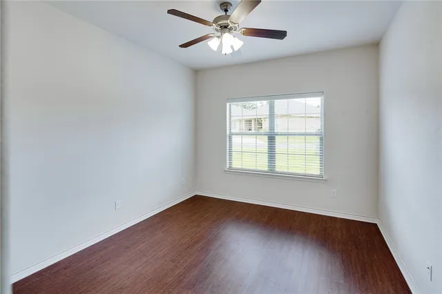 an empty room with wooden floor ceiling fan and windows