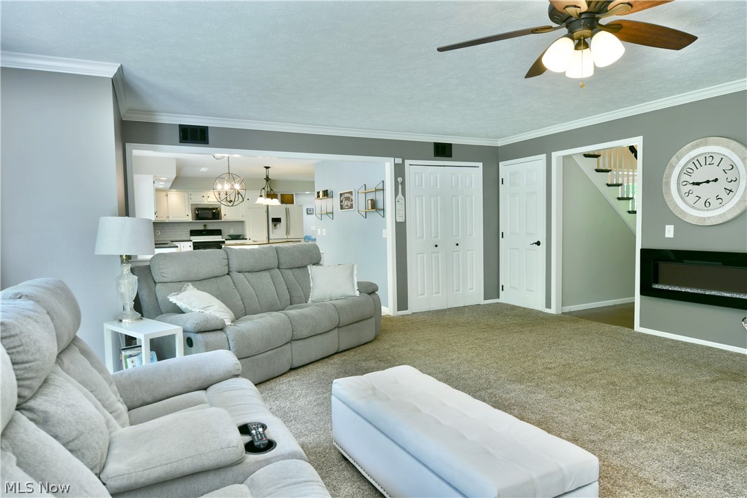 13491 Woodin Road Chardon, OH 44024 - Photo 17 of 35 Carpeted living room with crown molding, a textured ceiling, and ceiling fan with notable chandelier