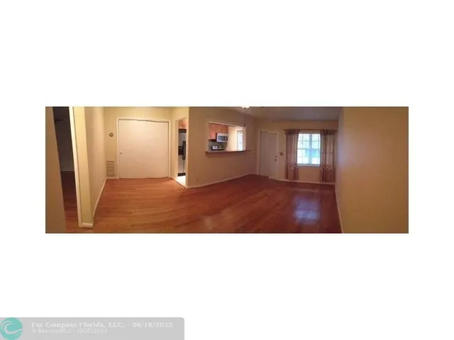 a view of an empty room with kitchen and a window