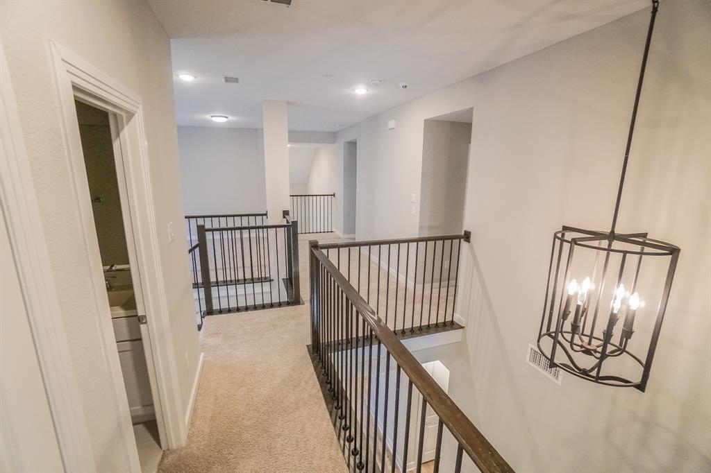 1309 Old Rocksprings Pass Mansfield, TX 76063 - Photo 20 of 36 Carpeted hallway with wrought iron railings and wood-finish banisters, illuminated by recessed lighting and a hanging geometric chandelier