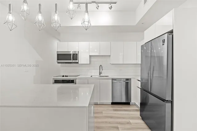 a kitchen with stainless steel appliances a stove top oven a sink dishwasher a refrigerator white cabinets and wooden floor