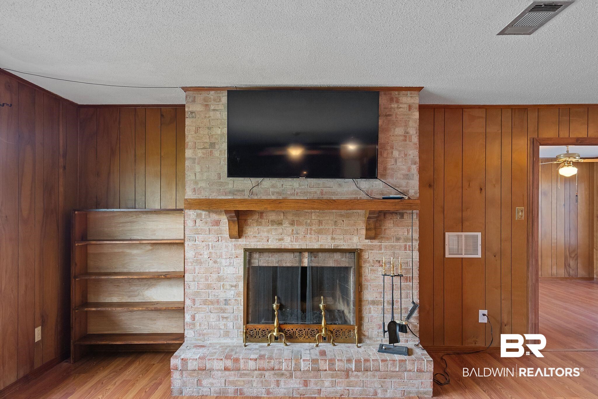 716 North Cedar Street Foley, AL 36535 - Photo 8 of 25 Brick fireplace with a wood mantle, complemented by built-in shelving, wood-finish flooring, and wood-paneled walls