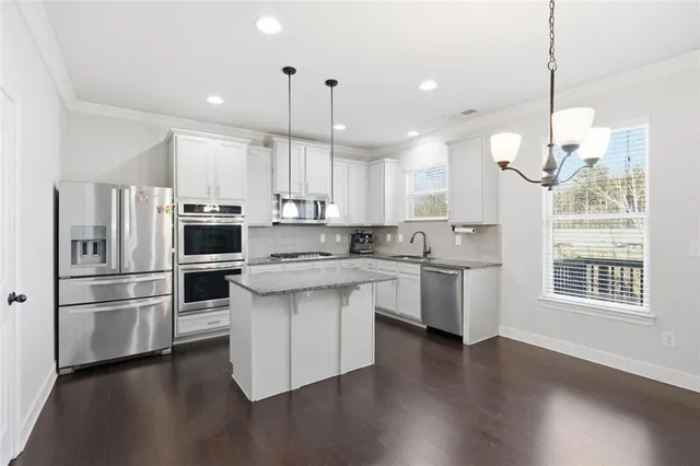 a kitchen with stainless steel appliances granite countertop a refrigerator a sink dishwasher a oven and a dining table with wooden floor