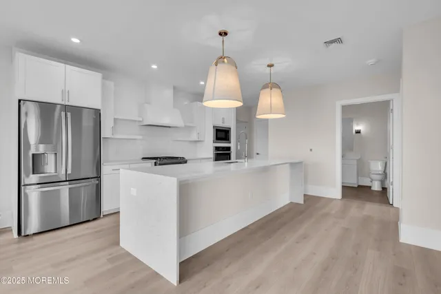 a kitchen with stainless steel appliances granite countertop a refrigerator a sink dishwasher a stove and white cabinets with wooden floor