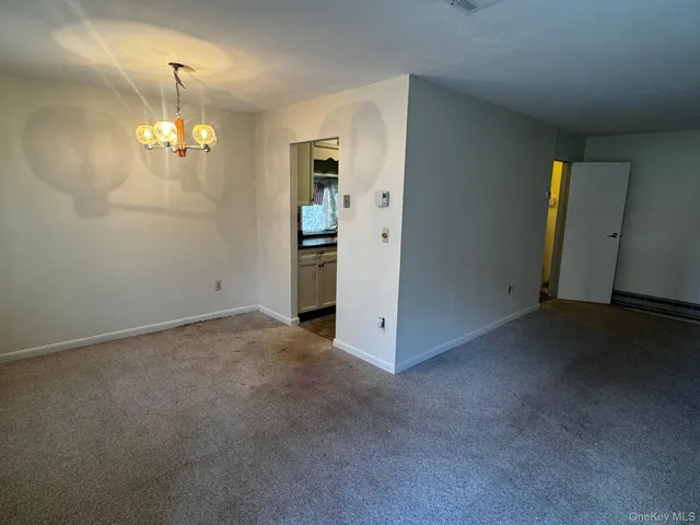 an empty room with kitchen view and a chandelier