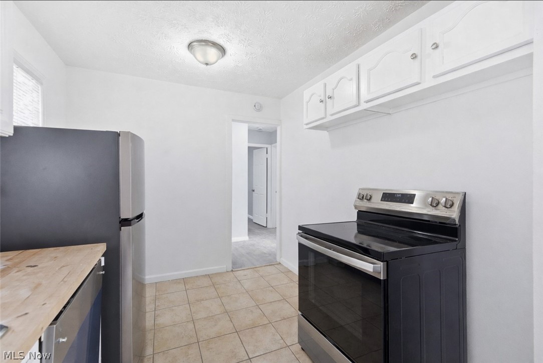 20705 Hansen Road Maple Heights, OH 44137 - Photo 7 of 24 Kitchen featuring stainless steel appliances, wooden counters, white cabinets, a textured ceiling, and light tile patterned flooring