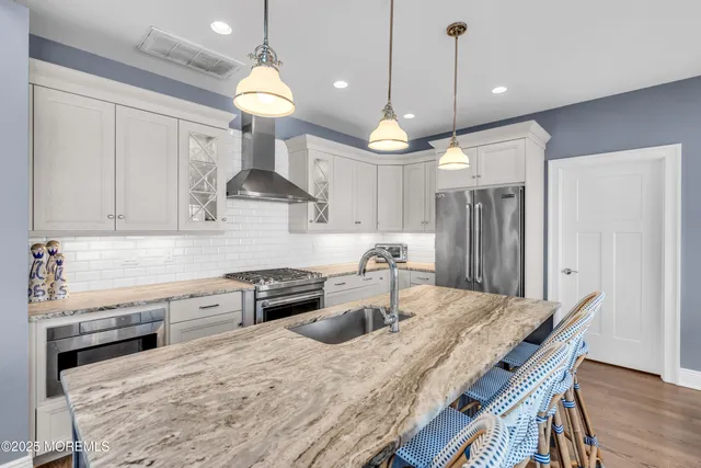 a kitchen with stainless steel appliances granite countertop a stove a refrigerator a sink a dining table and chairs with wooden floor