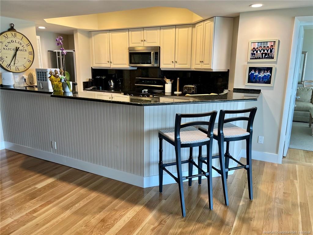 579 Northeast Plantation Road, Unit 301N Jensen Beach, FL 34957 - Photo 2 of 15 a kitchen with stainless steel appliances granite countertop a stove top oven a sink a dining table and chairs with wooden floor
