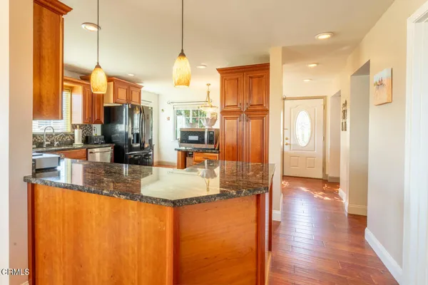 a view of a kitchen with kitchen island granite countertop a refrigerator a stove and a sink with wooden floor