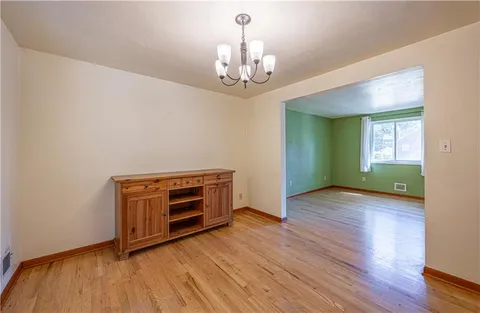 a view of an empty room with wooden floor kitchen view and a window