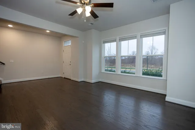 an empty room with wooden floor chandelier fan and windows