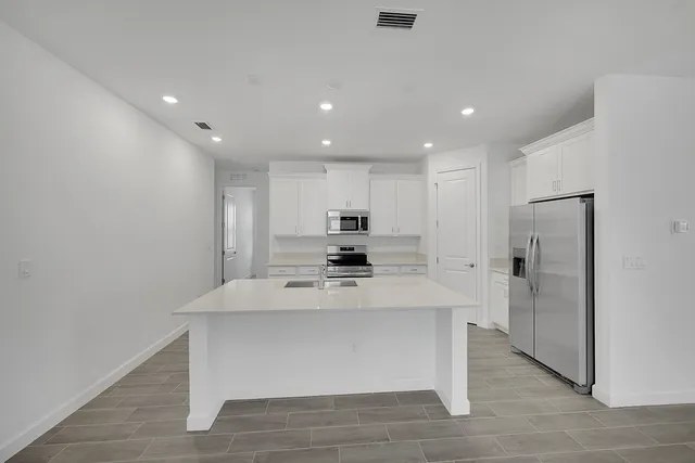 a large kitchen with stainless steel appliances a large counter top and a refrigerator