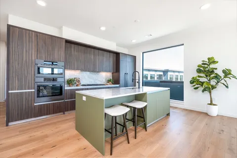 a kitchen with stainless steel appliances granite countertop a refrigerator a sink a stove a dining table and chairs with wooden floor